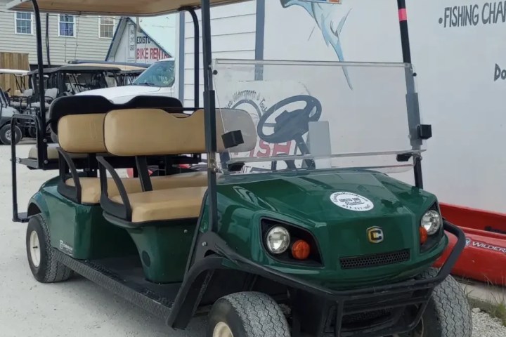 Green golf cart with beige seats parked beside a building.