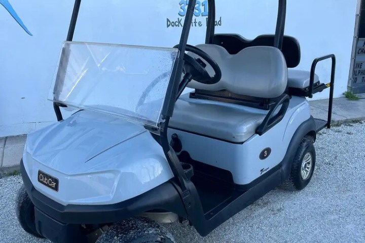 Gray golf cart parked on gravel in front of a building with signage.