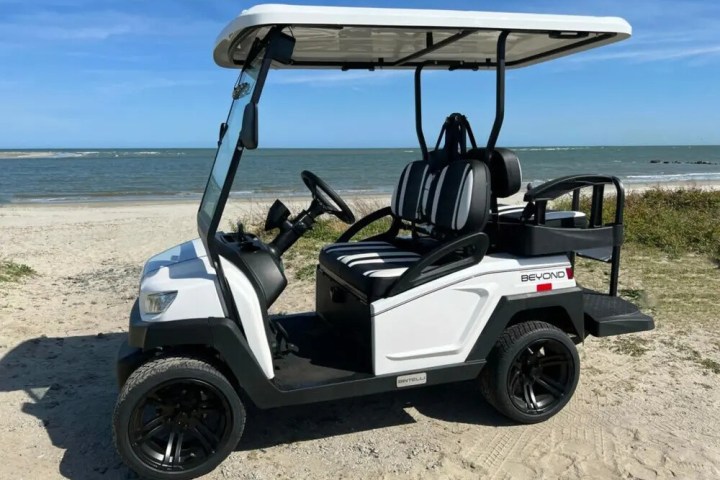 White golf cart on sandy beach by the ocean on a sunny day.